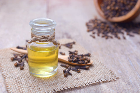 A small glass bottle of yellow oil sits on a wooden table with clove buds