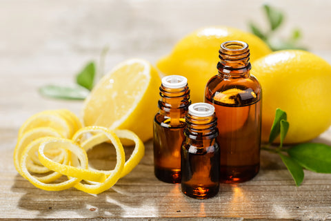 Three small amber-colored bottle sit on a wooden table with lemons and lemon rinds