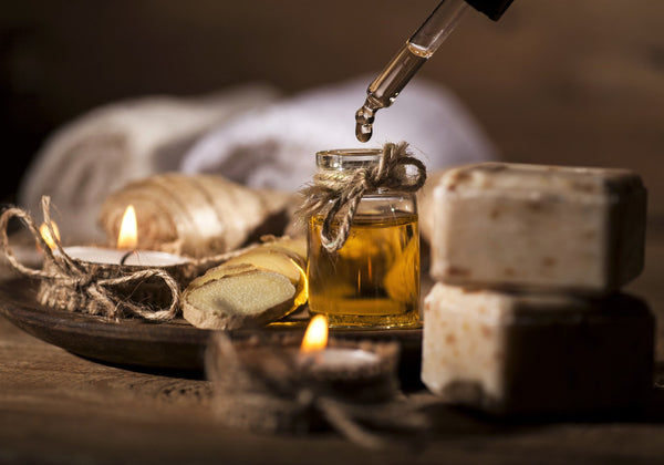 Lit tea candles surround a small bottle of oil, pieces of ginger, and bars of soap