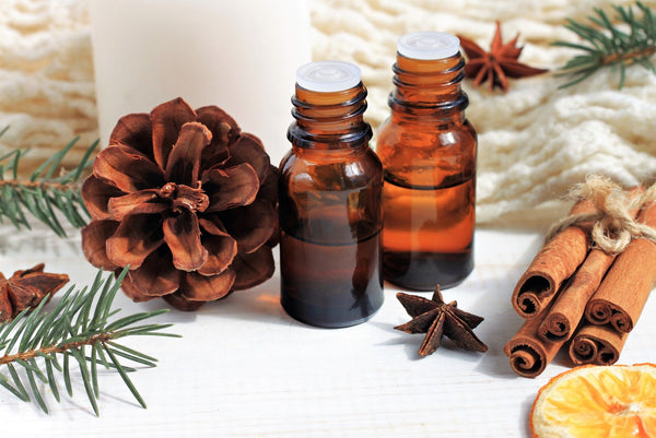 Two amber-colored bottles filled with oil sitting on a table surrounded by a pinecone and cinnamon sticks